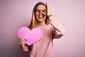 Young beautiful blonde romantic woman wearing glasses holding big pink heart with happy face smiling doing ok sign with hand on Royalty Free Stock Photo