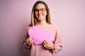 Young beautiful blonde romantic woman wearing glasses holding big pink heart with a happy face standing and smiling with a Royalty Free Stock Photo