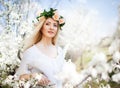 Young beautiful blonde smiling woman in white dress and rose wreath standing in blooming trees and looking aside Royalty Free Stock Photo