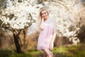 Young beautiful blonde smiling woman in white mini dress standing with blooming trees at background Royalty Free Stock Photo