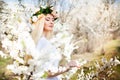 Young beautiful blonde smiling woman in white mini dress standing with blooming trees at background Royalty Free Stock Photo