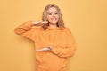 Young beautiful blonde sporty woman wearing casual sweatshirt over yellow background gesturing with hands showing big and large Royalty Free Stock Photo
