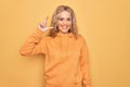 Young beautiful blonde sporty woman wearing casual sweatshirt over yellow background smiling and confident gesturing with hand Royalty Free Stock Photo