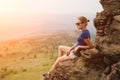 Young beautiful blonde tourist girl sits on a rocky ledge of a rock and looks far into the distance in the early foggy morning Royalty Free Stock Photo