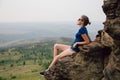 Young beautiful blonde tourist girl sits on a rocky ledge of a rock Royalty Free Stock Photo