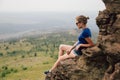 Young beautiful blonde tourist girl sits on a rocky ledge of a rock Royalty Free Stock Photo