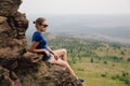 Young beautiful blonde tourist girl sits on a rocky ledge of a rock Royalty Free Stock Photo