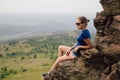 Young beautiful blonde tourist girl sits on a rocky ledge of a rock Royalty Free Stock Photo