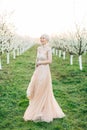 Young beautiful blonde woman in blooming garden. Pretty bride in elegant peach dress, posing on the background of