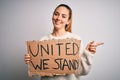 Young beautiful blonde woman with blue eyes asking for united stand holding banner very happy pointing with hand and finger to the