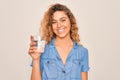 Young beautiful blonde woman with blue eyes drinking glass of water over white background with a happy face standing and smiling Royalty Free Stock Photo