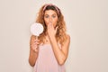 Young beautiful blonde woman with blue eyes eating sweet candy lollipop over pink background cover mouth with hand shocked with Royalty Free Stock Photo