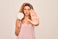 Young beautiful blonde woman with blue eyes eating sweet candy lollipop over pink background with open hand doing stop sign with Royalty Free Stock Photo