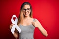 Young beautiful blonde woman with blue eyes holding white ribbon over red background happy with big smile doing ok sign, thumb up Royalty Free Stock Photo