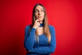 Young beautiful blonde woman with blue eyes standing over red background with hand on chin thinking about question, pensive Royalty Free Stock Photo