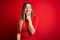 Young beautiful blonde woman with blue eyes wearing casual t-shirt over red background with hand on chin thinking about question, Royalty Free Stock Photo