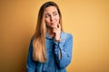 Young beautiful blonde woman with blue eyes wearing denim shirt over yellow background with hand on chin thinking about question, Royalty Free Stock Photo