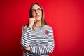 Young beautiful blonde woman with blue eyes wearing glasses standing over red background with hand on chin thinking about Royalty Free Stock Photo