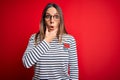 Young beautiful blonde woman with blue eyes wearing glasses standing over red background Looking fascinated with disbelief,