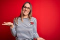 Young beautiful blonde woman with blue eyes wearing glasses standing over red background smiling cheerful with open arms as Royalty Free Stock Photo