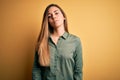Young beautiful blonde woman with blue eyes wearing green shirt over yellow background Relaxed with serious expression on face Royalty Free Stock Photo