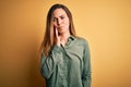 Young beautiful blonde woman with blue eyes wearing green shirt over yellow background touching mouth with hand with painful Royalty Free Stock Photo