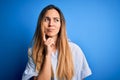 Young beautiful blonde woman with blue eyes wearing striped shirt over blue background with hand on chin thinking about question, Royalty Free Stock Photo