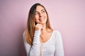 Young beautiful blonde woman with blue eyes wearing white t-shirt over pink background with hand on chin thinking about question, Royalty Free Stock Photo