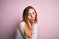 Young beautiful blonde woman with blue eyes wearing white t-shirt over pink background hand on mouth telling secret rumor, Royalty Free Stock Photo