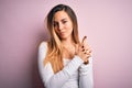 Young beautiful blonde woman with blue eyes wearing white t-shirt over pink background Holding symbolic gun with hand gesture, Royalty Free Stock Photo