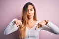 Young beautiful blonde woman with blue eyes wearing white t-shirt over pink background Pointing down looking sad and upset, Royalty Free Stock Photo