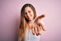 Young beautiful blonde woman with blue eyes wearing white t-shirt over pink background smiling cheerful offering palm hand giving Royalty Free Stock Photo