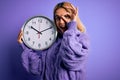 Young beautiful blonde woman doing countdown holding big clock over purple background with happy face smiling doing ok sign with Royalty Free Stock Photo