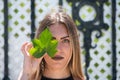 Young, beautiful blonde woman dressed in black covers one eye with a green ivy leaf and looks straight ahead. Fashion and beauty Royalty Free Stock Photo