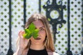 Young, beautiful blonde woman dressed in black covers one eye with a green ivy leaf and looks straight ahead. Fashion and beauty Royalty Free Stock Photo