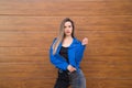 young and beautiful blonde woman dressed in black t-shirt and blue leather jacket and jeans on wooden background poses for photos Royalty Free Stock Photo