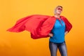 Young and beautiful blonde woman dressed like superheroine with red cape in the air.