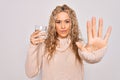 Young beautiful blonde woman drinking glass of water over isolated white background with open hand doing stop sign with serious Royalty Free Stock Photo