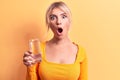Young beautiful blonde woman drinking glass of water over isolated yellow background scared and amazed with open mouth for Royalty Free Stock Photo