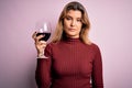 Young beautiful blonde woman drinking glasse of red wine over isolated pink background with a confident expression on smart face Royalty Free Stock Photo