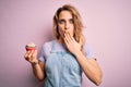 Young beautiful blonde woman eatimg chocolate cupcake over  pink background cover mouth with hand shocked with shame for Royalty Free Stock Photo