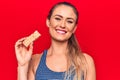 Young beautiful blonde woman eating muesli cereal bar over isolated red background looking positive and happy standing and smiling Royalty Free Stock Photo
