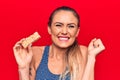 Young beautiful blonde woman eating muesli cereal bar over isolated red background screaming proud, celebrating victory and Royalty Free Stock Photo