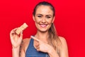 Young beautiful blonde woman eating muesli cereal bar over isolated red background smiling happy pointing with hand and finger Royalty Free Stock Photo