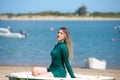 Young, beautiful blonde woman in an elegant green dress is sitting in a green fisherman's boat on the seashore. Royalty Free Stock Photo