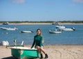 Young, beautiful blonde woman in an elegant green dress is sitting in a green fisherman's boat on the seashore. In the background Royalty Free Stock Photo