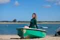 Young, beautiful blonde woman in an elegant green dress is sitting in a green fisherman's boat on the seashore. In the background Royalty Free Stock Photo