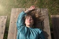 Young, beautiful, blonde woman in green shirt, eyes closed lying on a wooden table sunbathing. Concept peace, tranquility, beauty Royalty Free Stock Photo