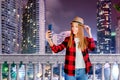 Young beautiful blonde woman in hat with smartphone on the night street. Urban portrait. Blogging