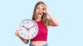 Young beautiful blonde woman holding big clock smiling happy doing ok sign with hand on eye looking through fingers Royalty Free Stock Photo